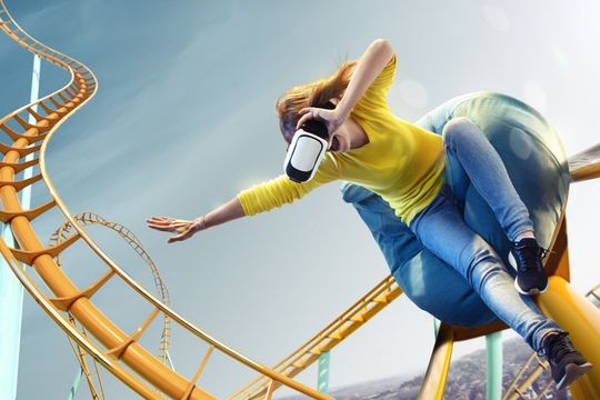 A woman wearing a virtual reality headset is riding a roller coaster.