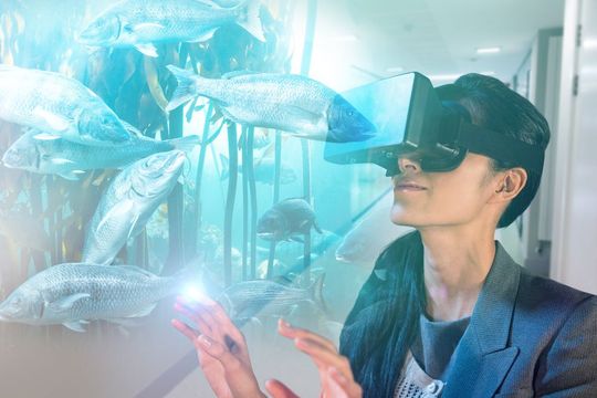 A man wearing a virtual reality headset is looking at fish in an aquarium.