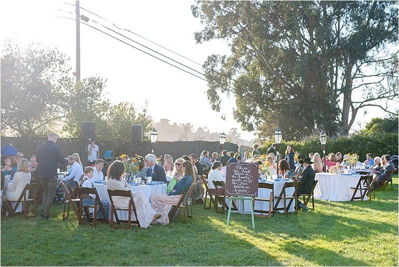 A large group of people are sitting at tables in a grassy field