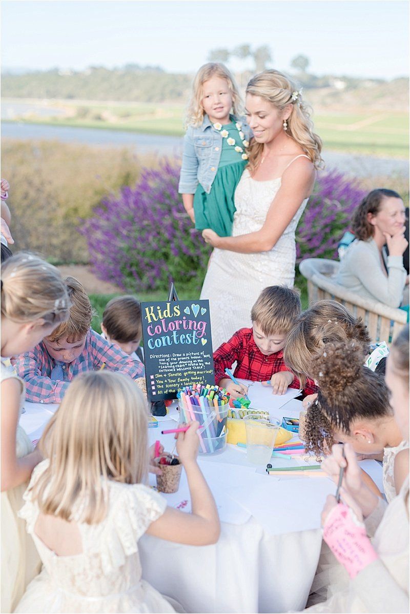 A bride and groom are standing next to a table with children sitting at it.