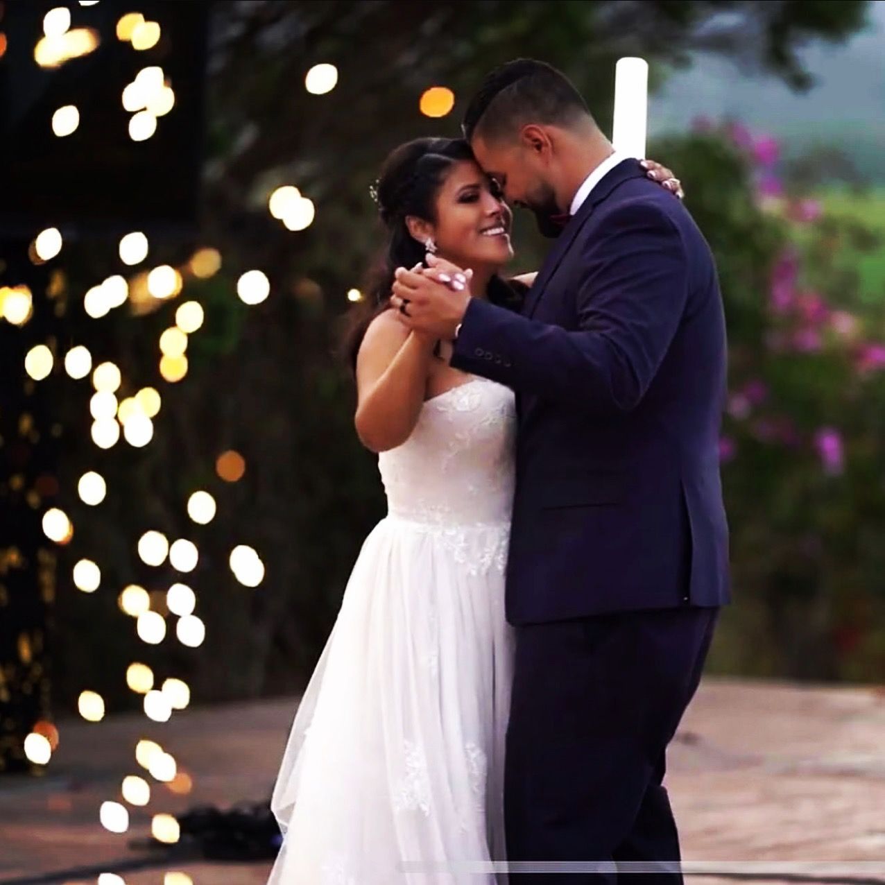 A bride and groom are dancing in front of a fireworks display