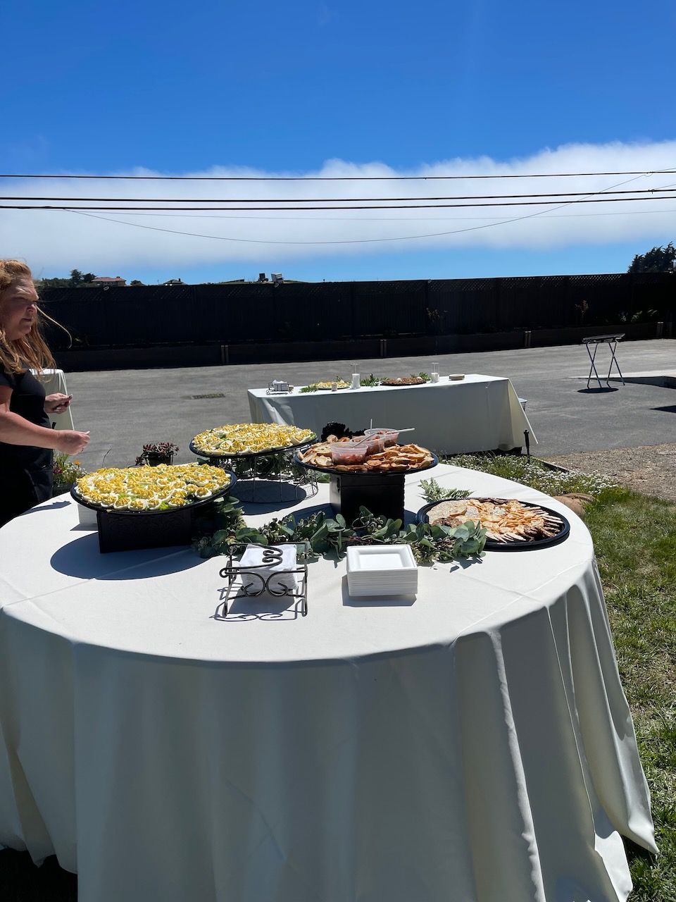 A woman is standing next to a table with plates of food on it.