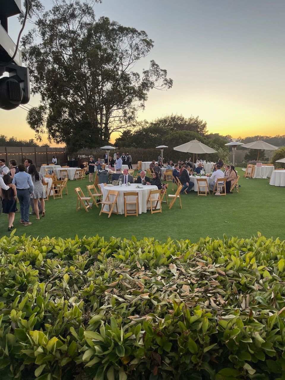 A group of people are sitting at tables on a lush green field.