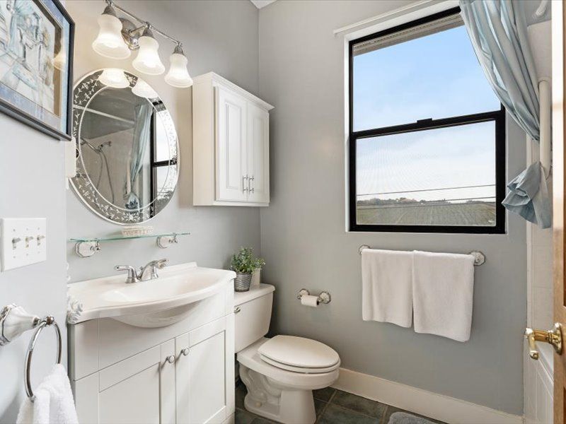 A bathroom with a sink , toilet , mirror and window.