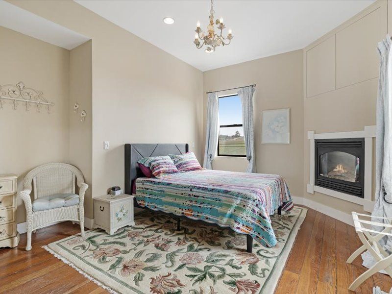 A bedroom with a bed , chair , nightstand , rug and fireplace.