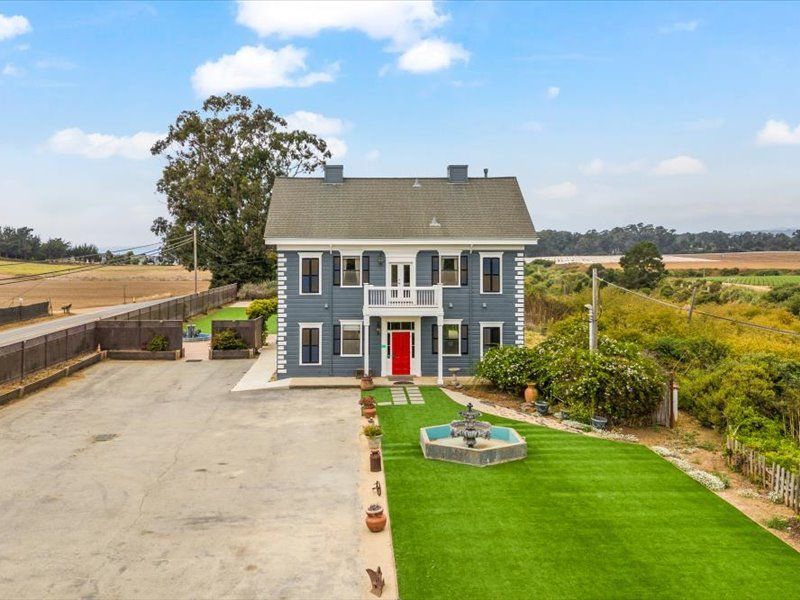 A large blue house with a red door and a fountain in front of it