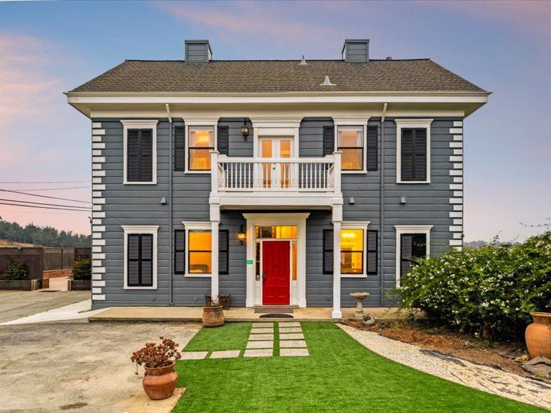A large gray house with a red door and a balcony.