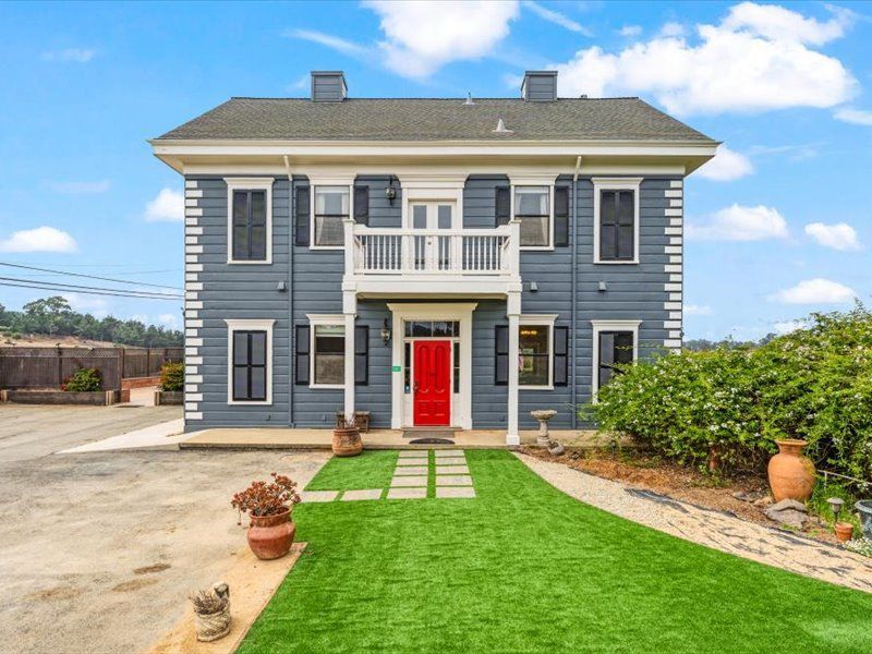 A large gray house with a red door and a green lawn in front of it.