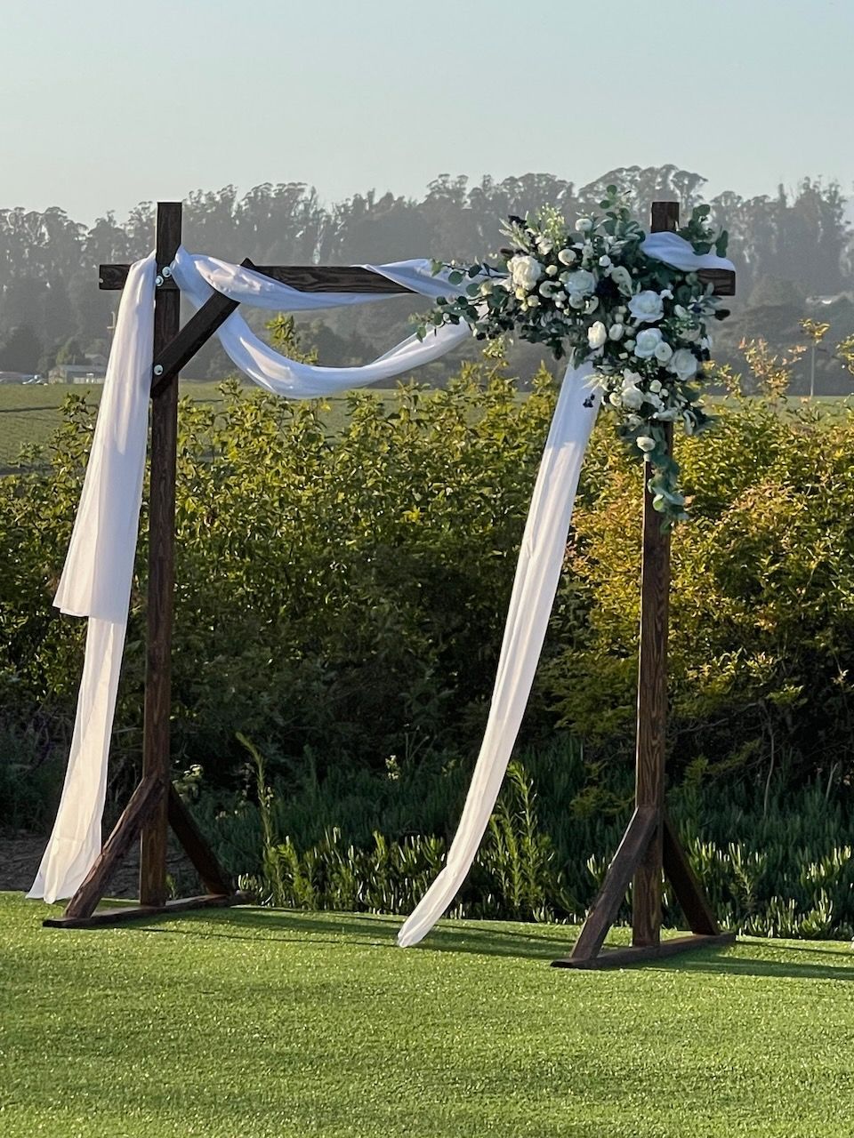 A wooden arch decorated with white flowers is sitting on top of a lush green field.
