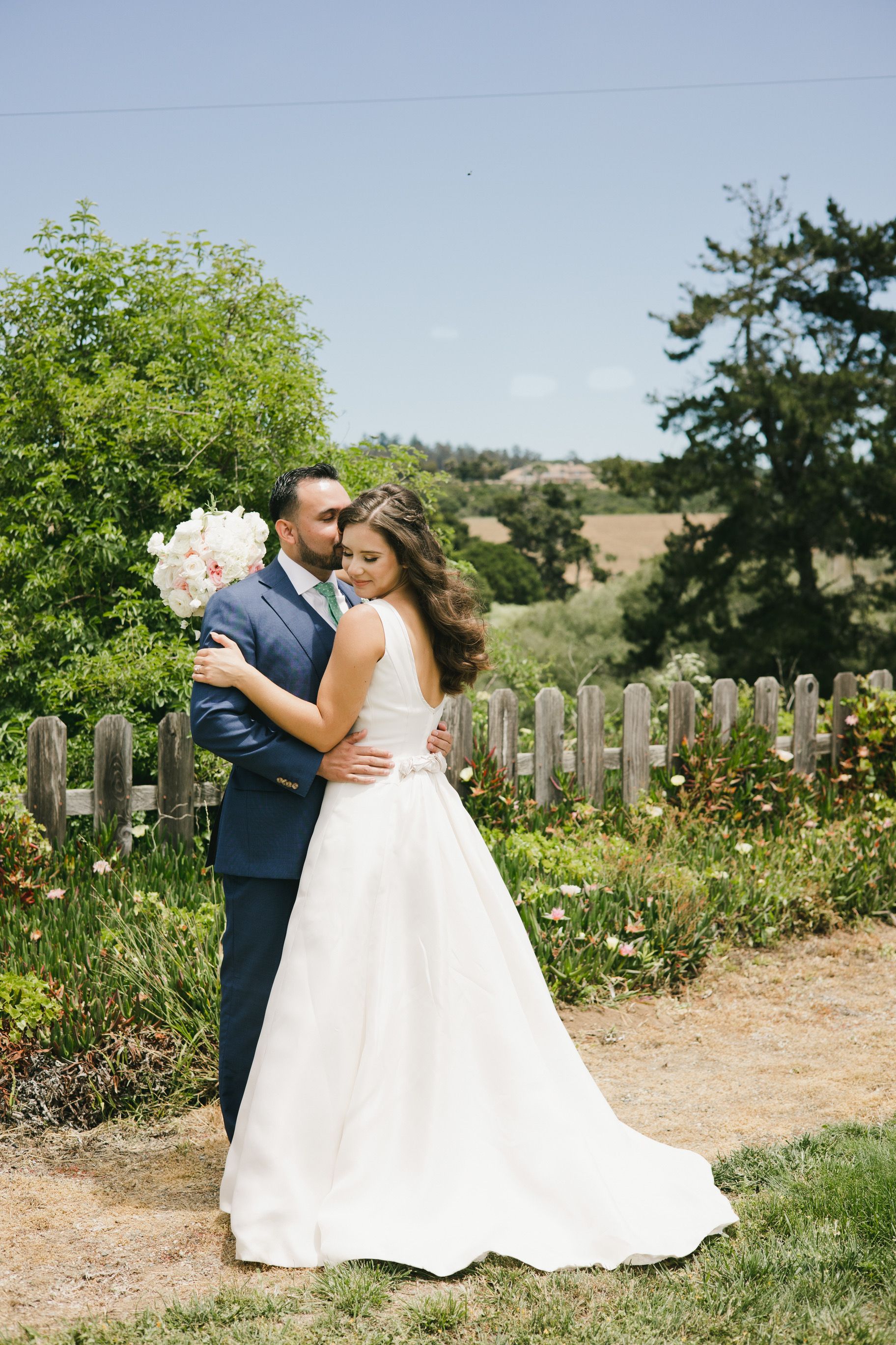 A bride and groom are posing for a picture in front of a wooden fence.