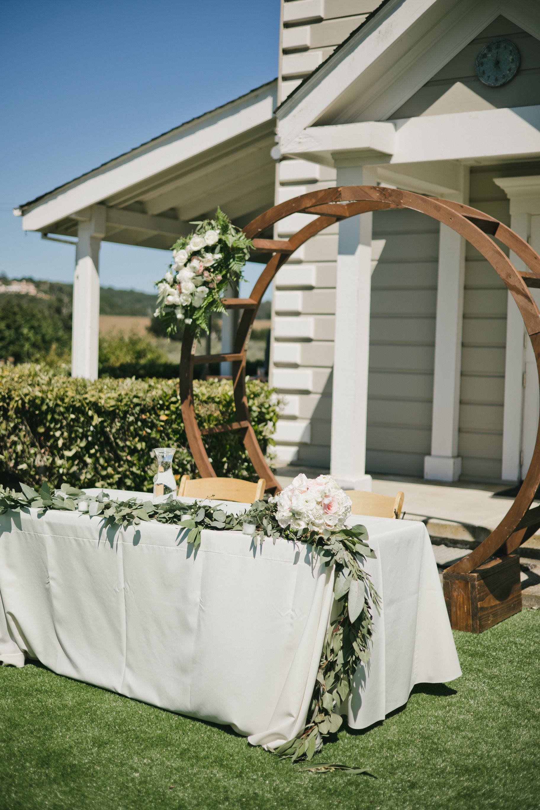 A table with a white tablecloth is sitting in the grass in front of a building.