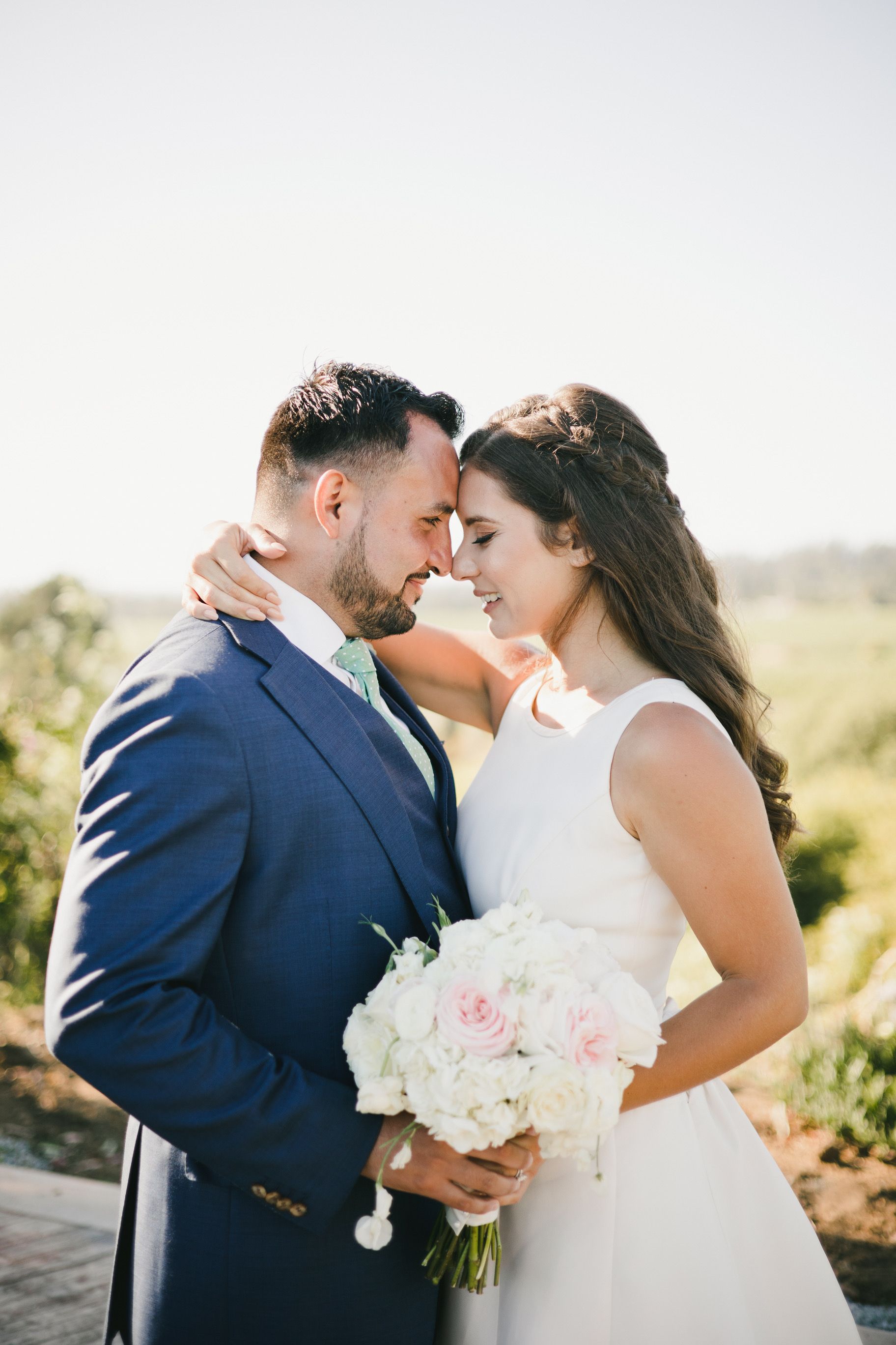 A bride and groom are looking into each other 's eyes while holding a bouquet of flowers.