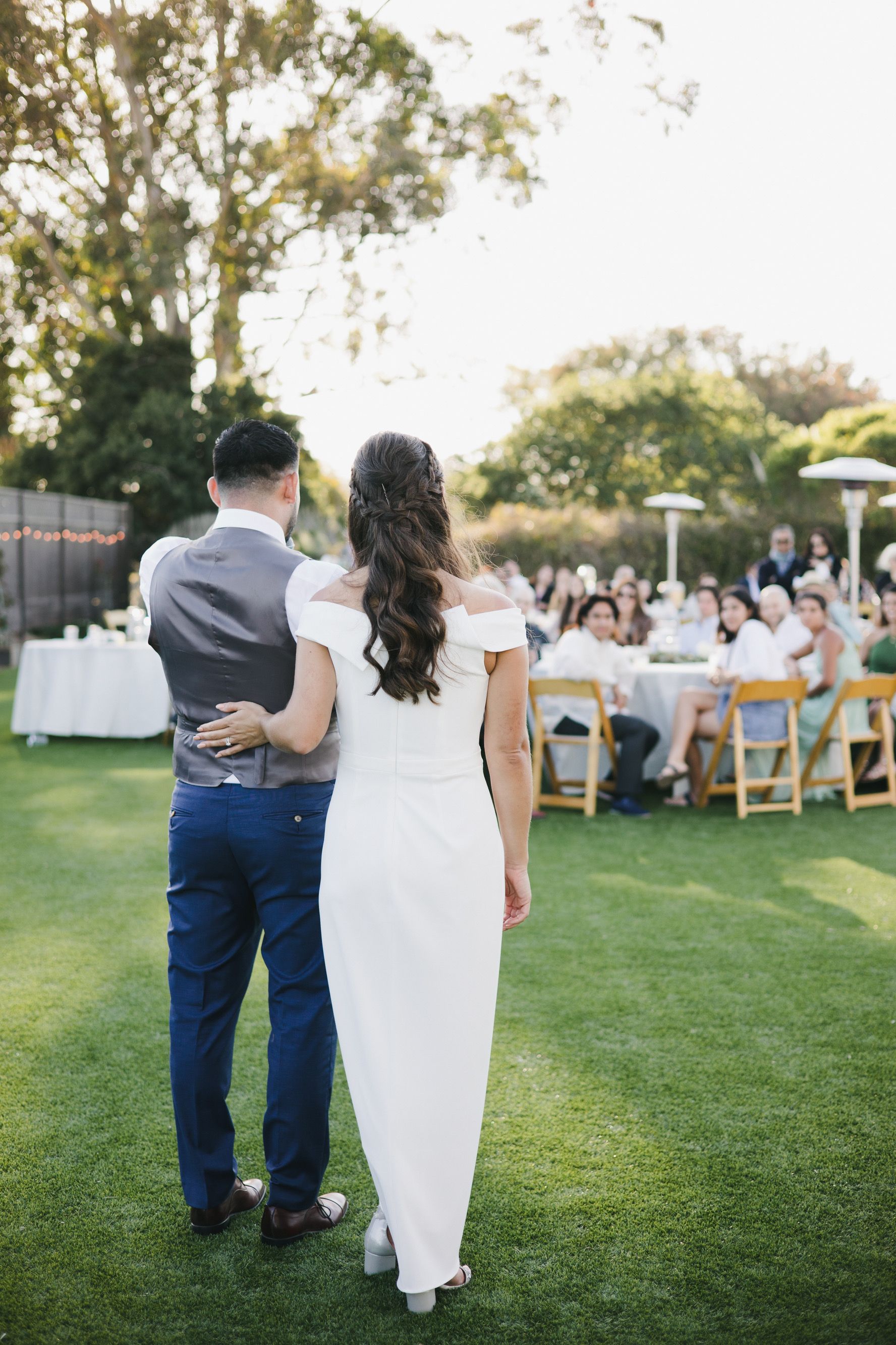 A bride and groom are standing next to each other on a lush green field at their wedding reception.