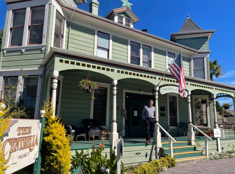A man stands on the porch of a green house