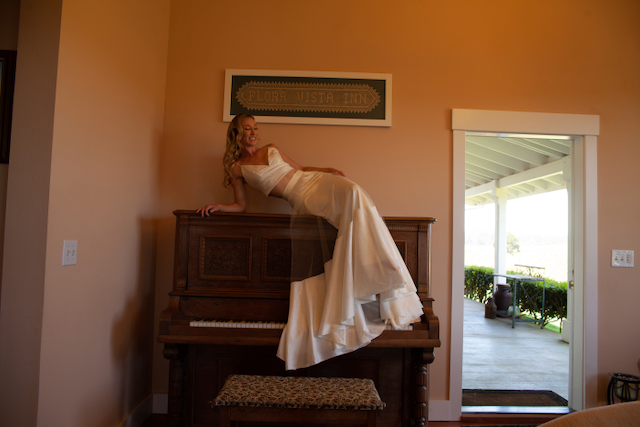 A woman in a wedding dress is sitting on a piano.