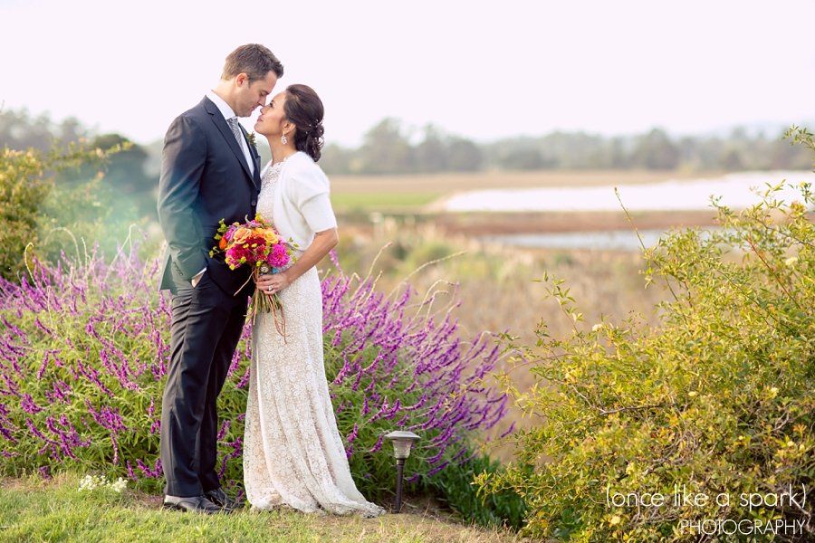 A bride and groom are kissing in front of purple flowers.