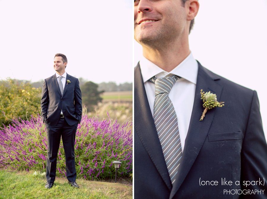 A man in a suit and tie is standing in front of purple flowers.