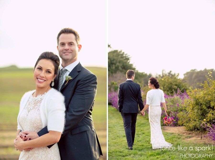 A bride and groom are walking in a field holding hands.