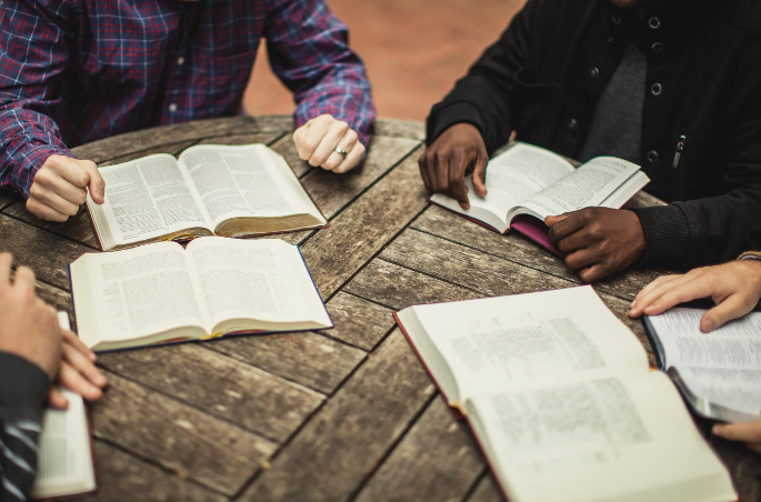 A group of people are sitting around a table reading books.