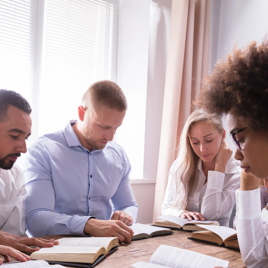 A group of people are sitting around a table reading books.