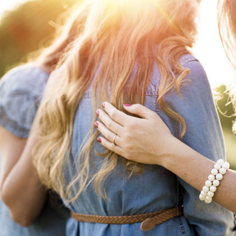 A woman wearing a pearl bracelet is hugging another woman