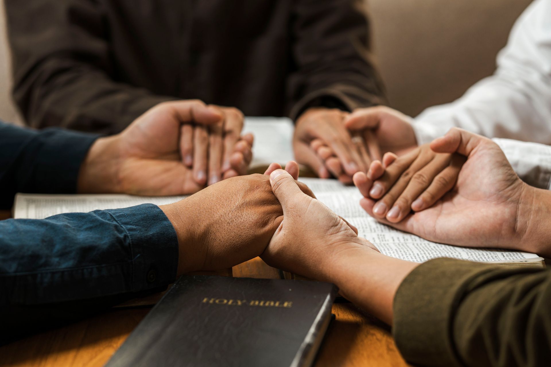 A group of people are holding hands over a bible.