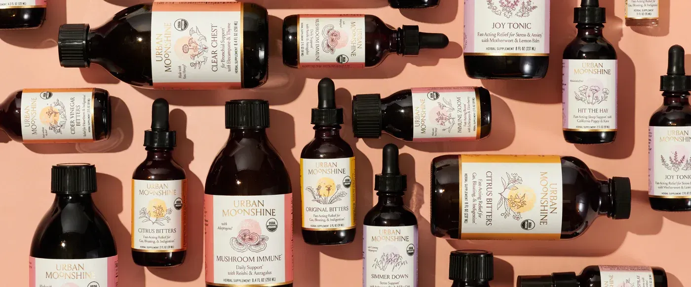 Assortment of brown glass bottles with white labels arranged on a pink background. Some bottles have droppers.