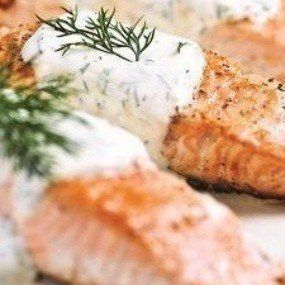 Pan-seared salmon topped with creamy dill sauce and fresh dill sprigs.