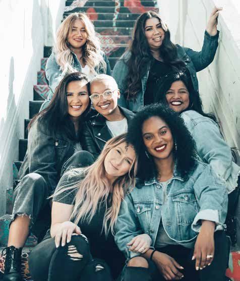 Group of seven women of diverse backgrounds sitting on colorful outdoor stairs, all wearing denim jackets.