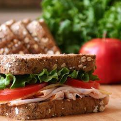 Sandwich with tomato, turkey, and lettuce on multi-grain bread, with an apple and lettuce in the background.
