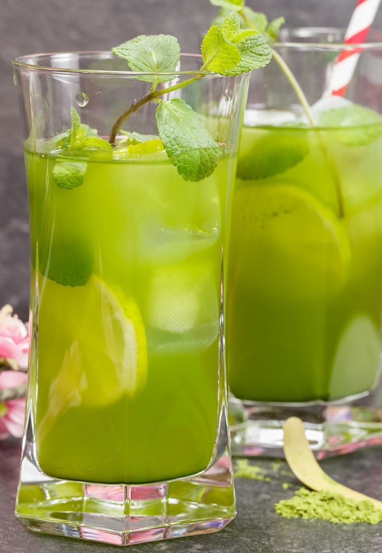 Two green matcha drinks with ice and mint leaves, garnished with lime slices, on a dark surface.