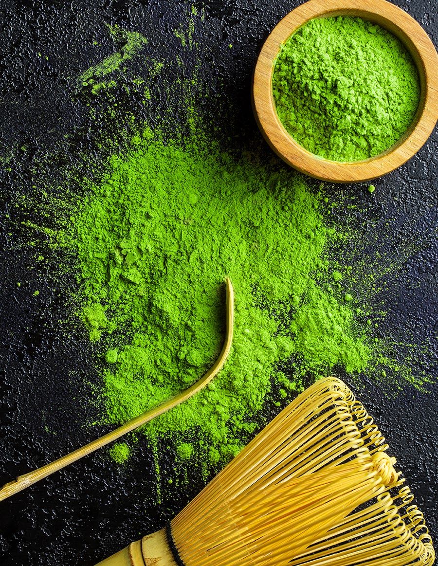 Matcha powder spilled on a dark surface with a bamboo whisk and bowl of matcha.