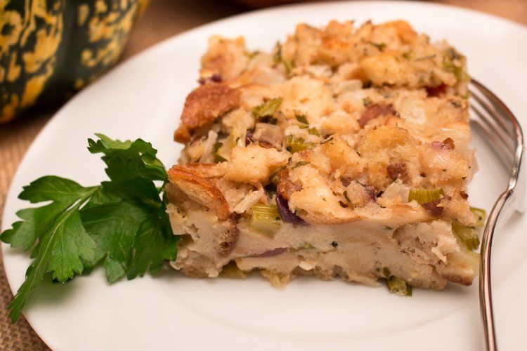 A square of baked stuffing on a white plate with a parsley sprig. A fork rests beside it.
