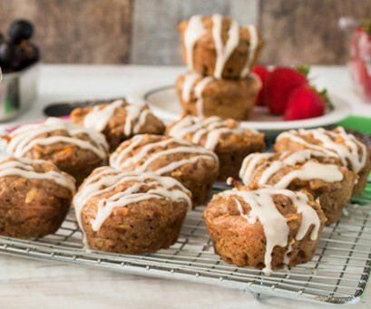 Carrot muffins with white glaze on a wire rack, alongside strawberries and grapes.