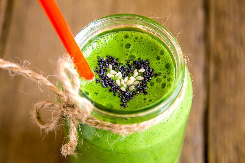 Green smoothie in a jar with a heart made of seeds, a red straw, and twine tied around the jar, on a wooden surface.