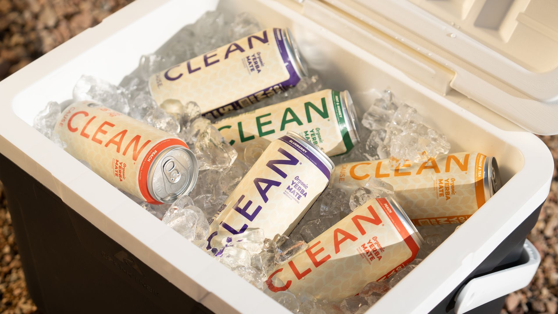 A cooler filled with ice and cans of CLEAN energy drink in various colors: red, purple, green, and gold.