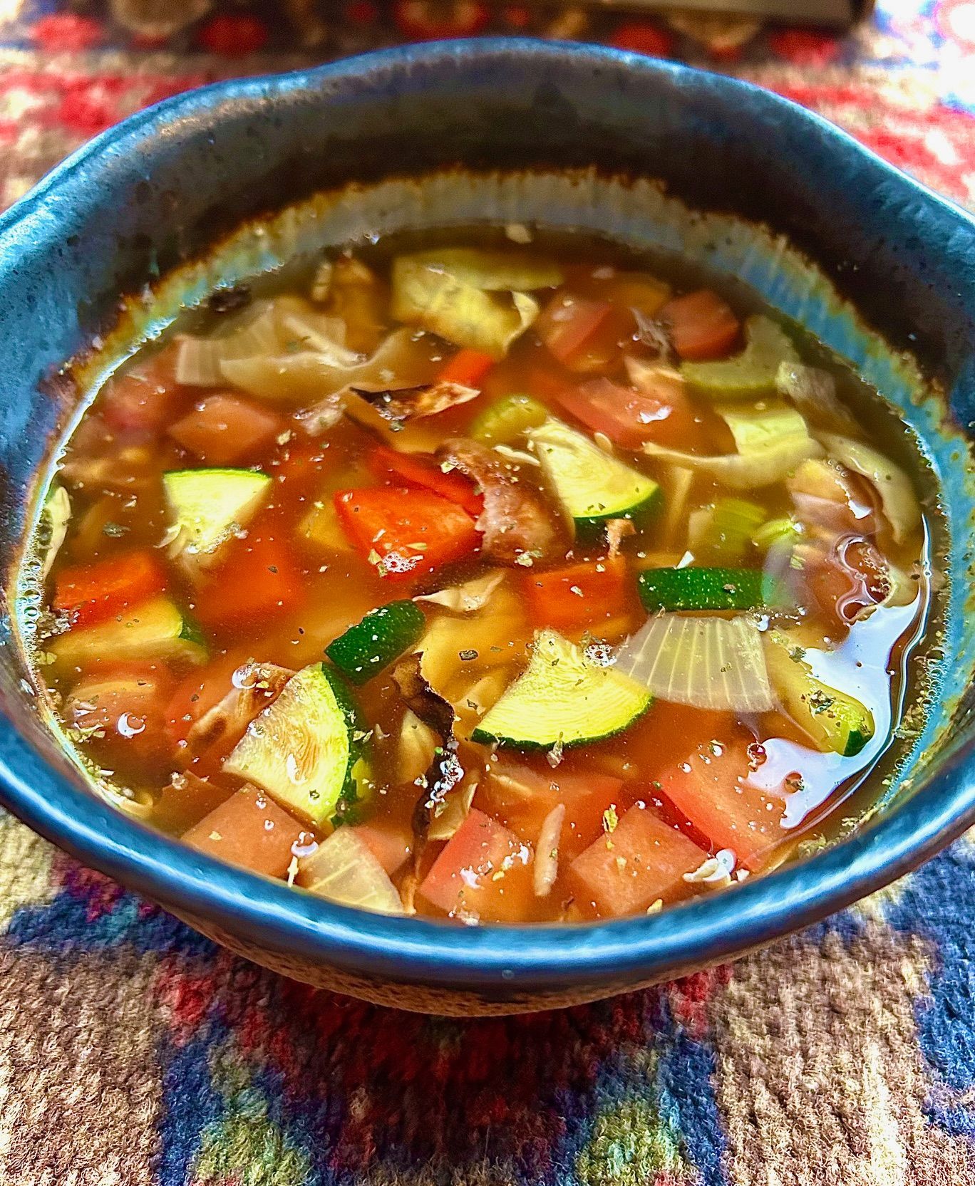 Vegetable soup in a blue bowl, featuring chopped zucchini, carrots, and tomatoes.