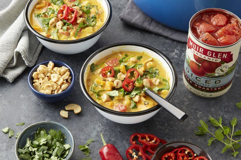 Bowls of yellow curry with vegetables and toppings, alongside ingredients like tomatoes and cashews.