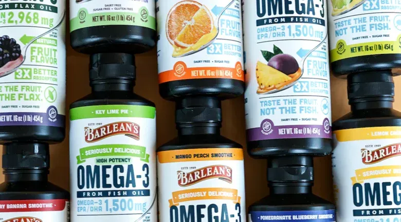 Close-up of several bottles of Barlean's Omega-3 fish oil in various fruit flavors stacked on top of each other.