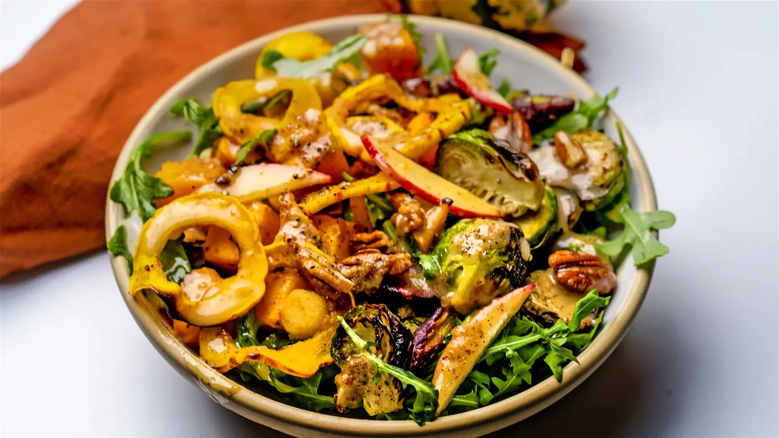Bowl of roasted vegetables and greens, including Brussels sprouts, yellow peppers, and arugula.