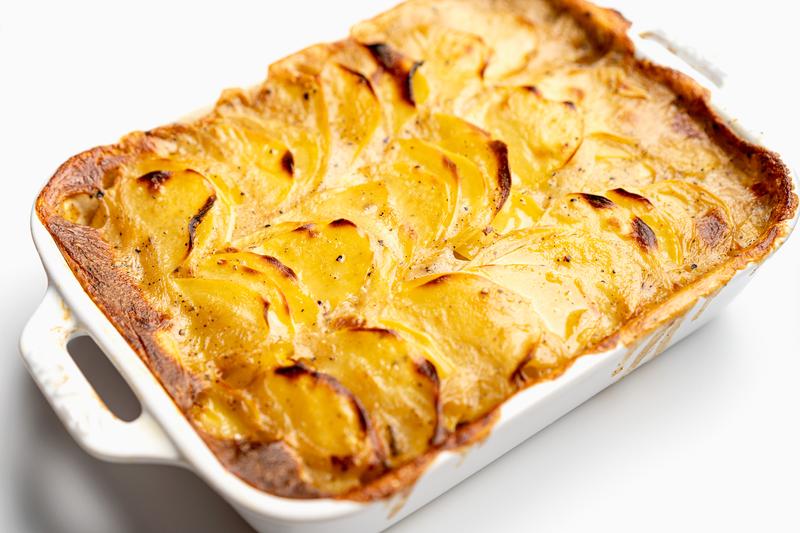 Scalloped potatoes in a white baking dish, golden-brown and bubbly from baking.