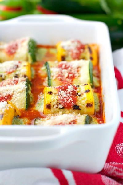 Zucchini roll-ups in a white baking dish, covered in tomato sauce and sprinkled with parmesan cheese.