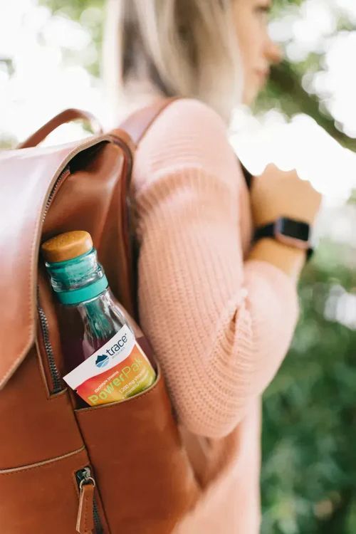 A woman with a backpack holding a juice bottle in its side pocket. The woman is wearing a pink sweater and a smartwatch.