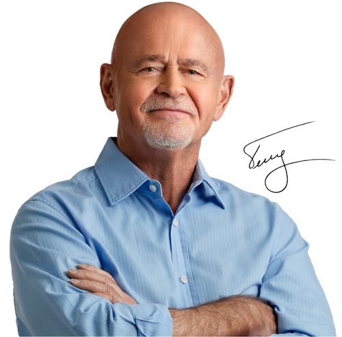 Bald man with a goatee, arms crossed, smiling in a blue button-down shirt. Signature 