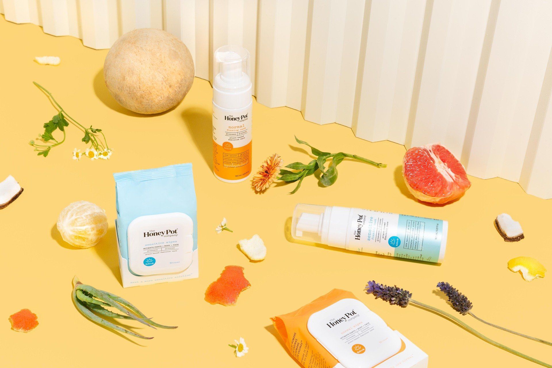 Cosmetics products and fruits, like grapefruit and coconut, arranged on a yellow surface.