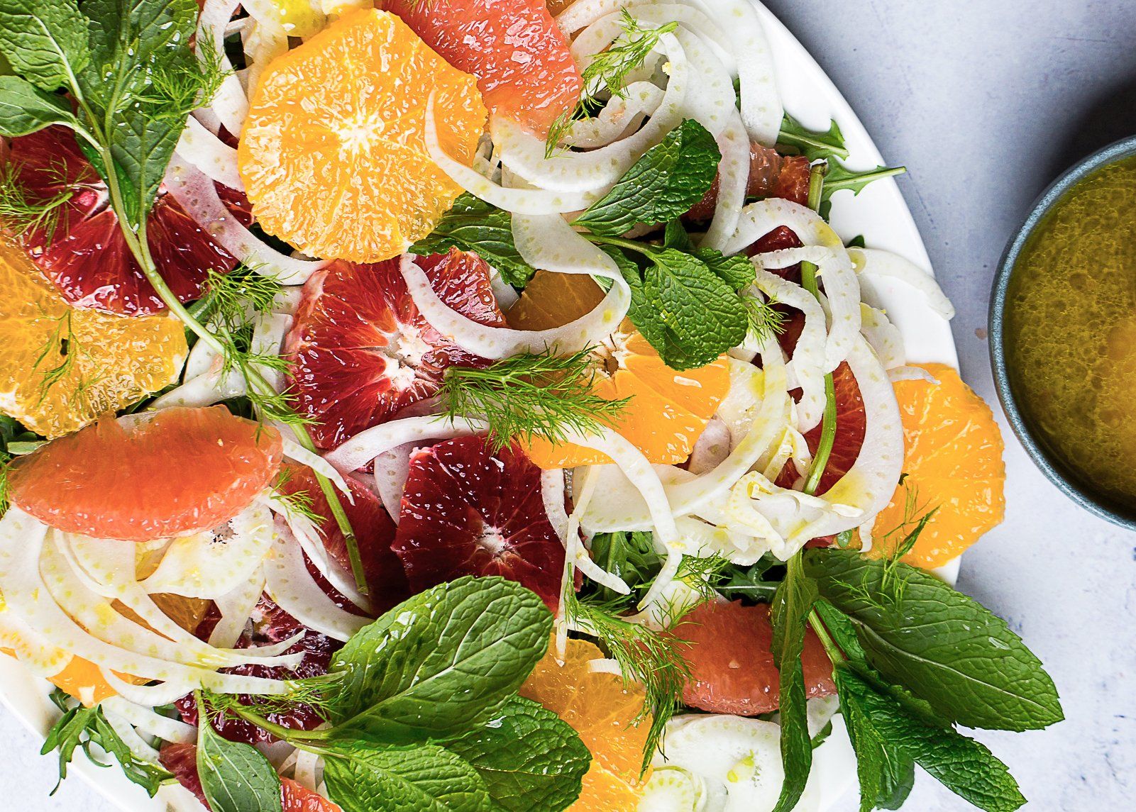 Citrus salad with orange, grapefruit, and fennel on a white plate, served with a green dressing.