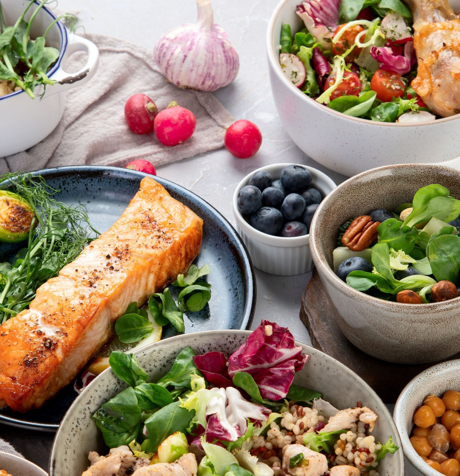 Assortment of healthy food: grilled salmon, salads with vegetables, blueberries, nuts, and chickpeas.  Fresh and colorful arrangement on a table.
