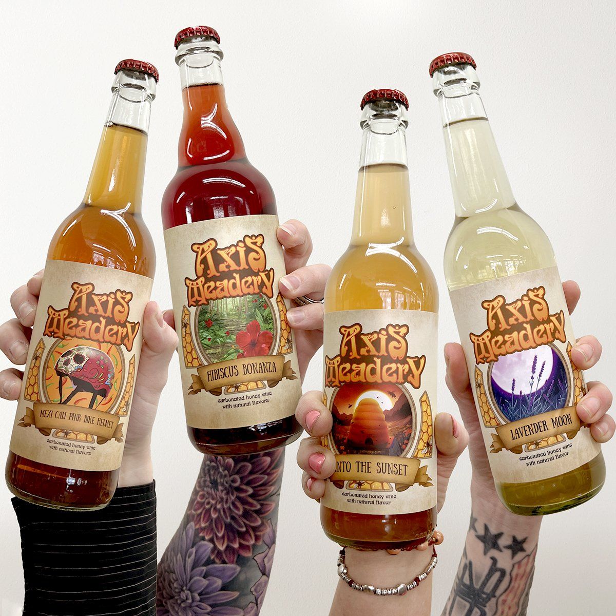 Four hands holding up bottles of Axis Meader, each with a different colored liquid and label.