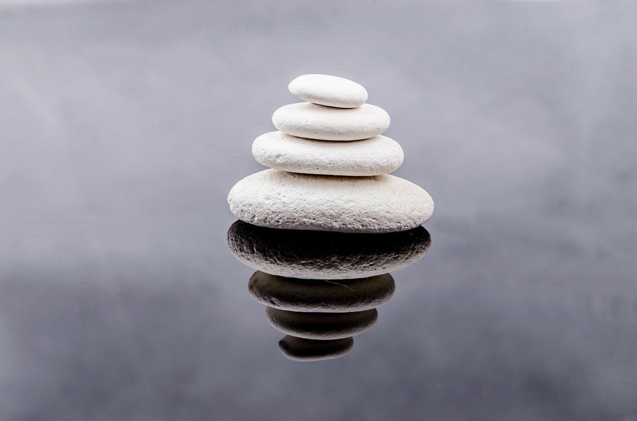 Stack of white, smooth stones balanced on a reflective surface, suggesting balance and serenity.