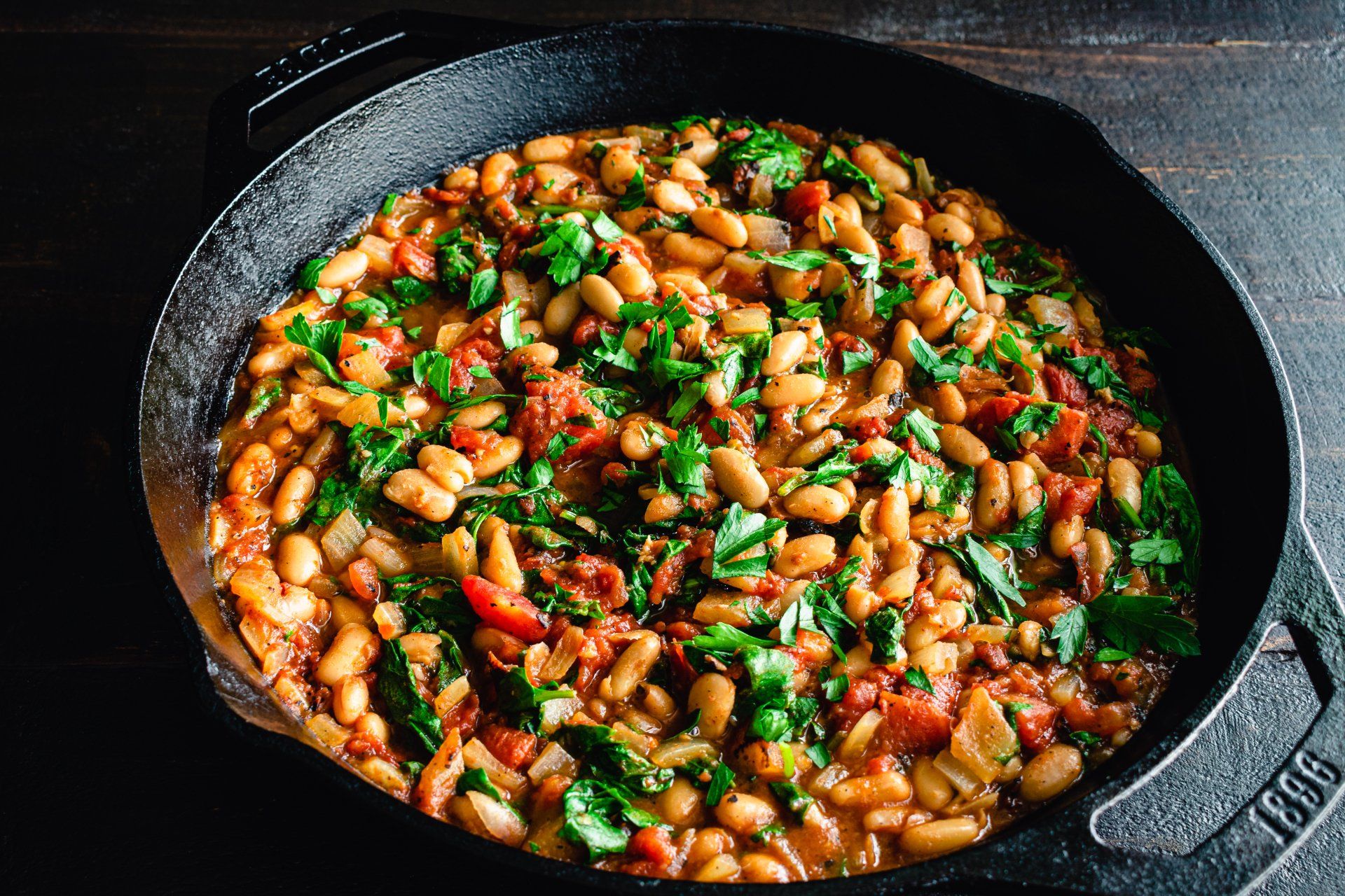 Cast iron skillet filled with white beans, tomatoes, and green herbs.